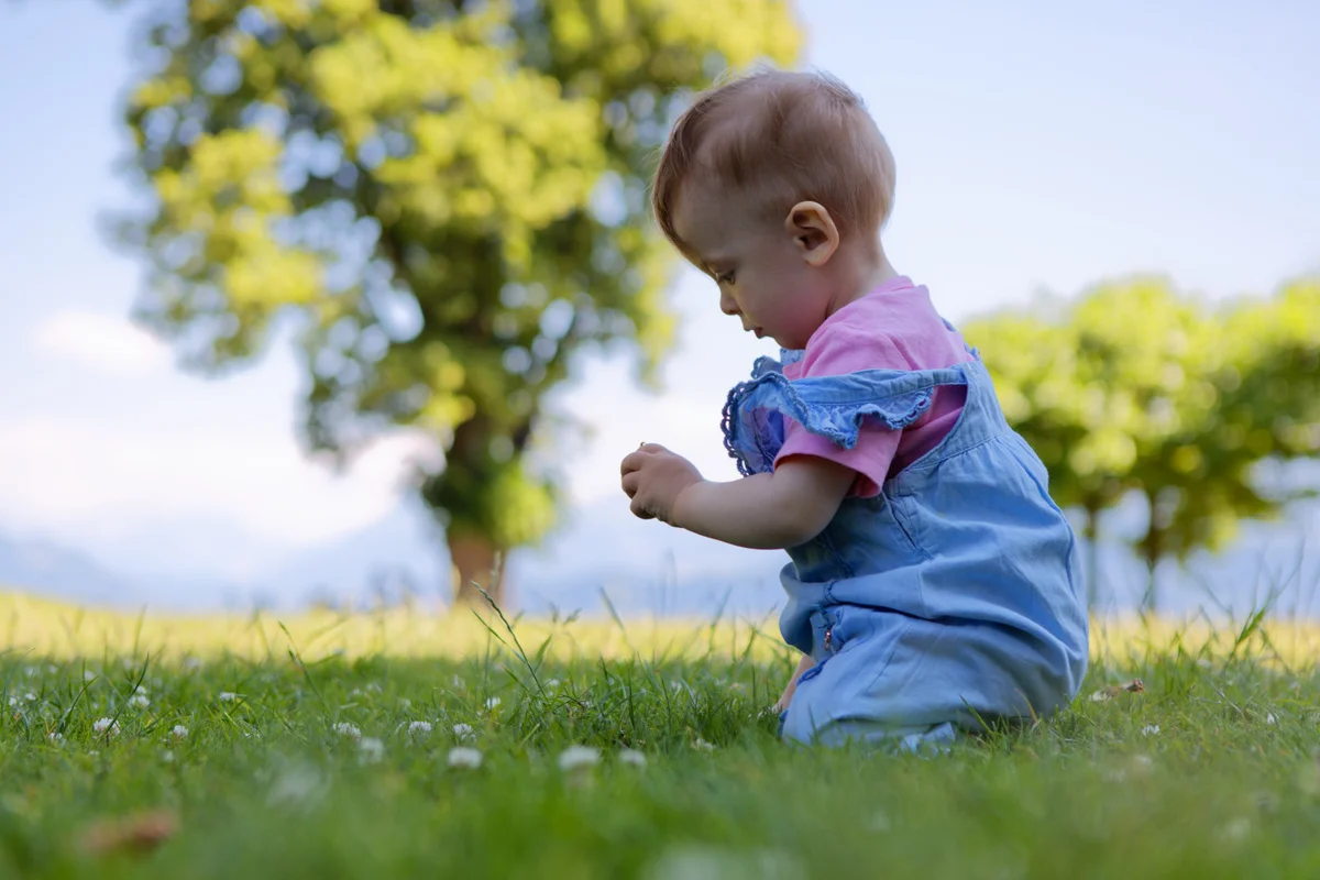 Babyfotografie Schweiz – Kleinkind sitzt im Gras und entdeckt die Natur
