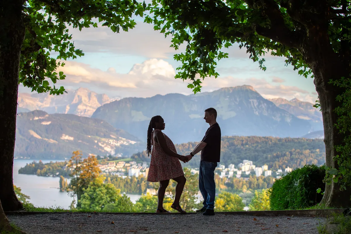 Babybauch Shooting Dreilindenpark – Paar hält Hände bei Sonnenuntergang vor Bergpanorama