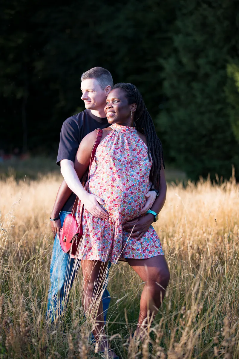 Babybauch Fotoshooting Dreilindenpark – Mann umarmt schwangere Partnerin auf der Wiese