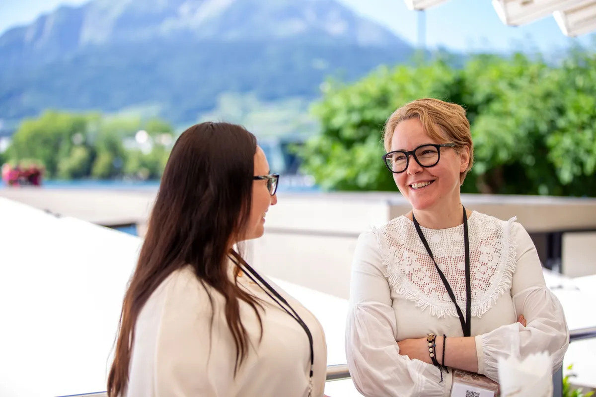 Networking-Pause auf der Terrasse des Grand Casino Luzern – zwei Frauen im Gespräch mit Pilatus-Panorama