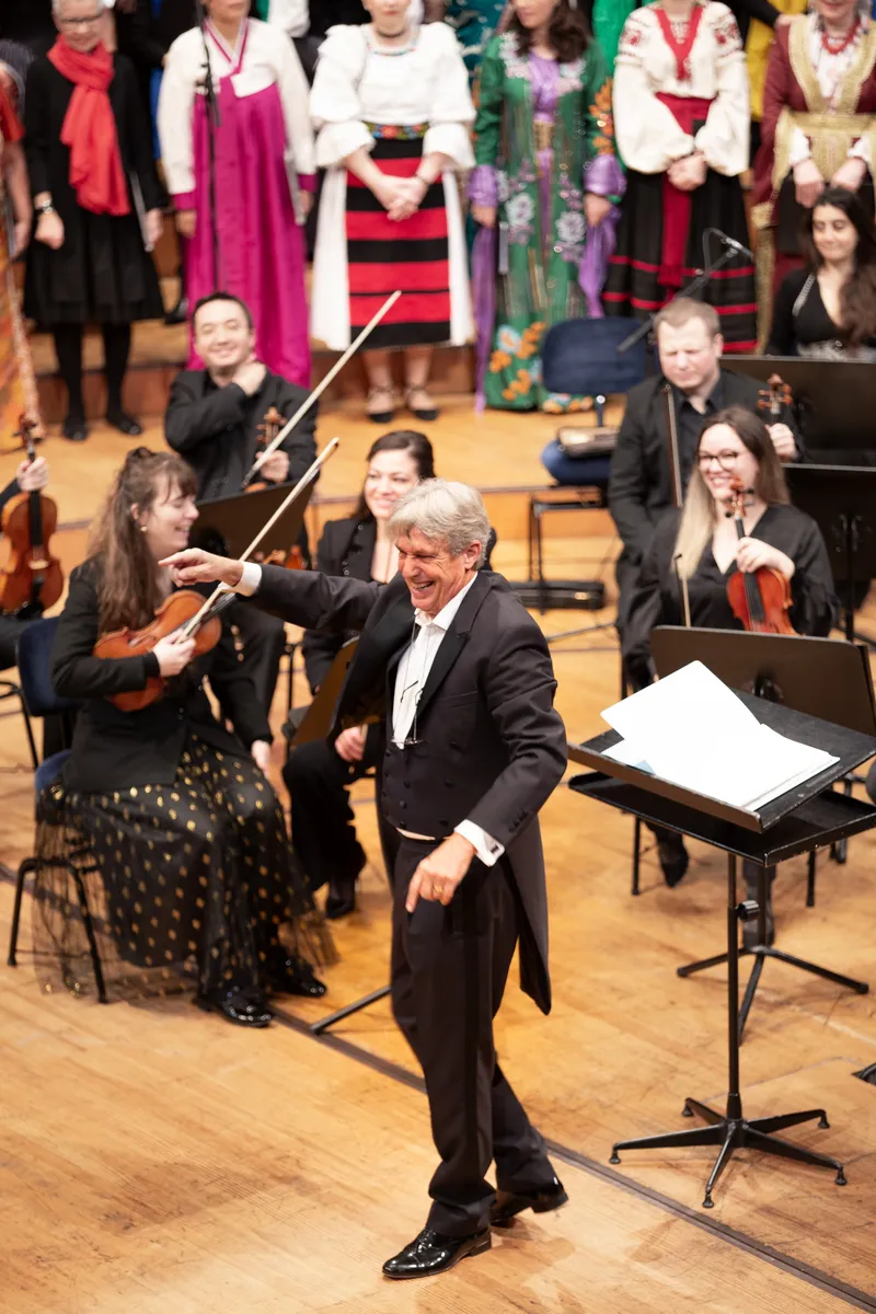 Konzertfotografie – lachender Dirigent zwischen den Musikerinnen und Musikern