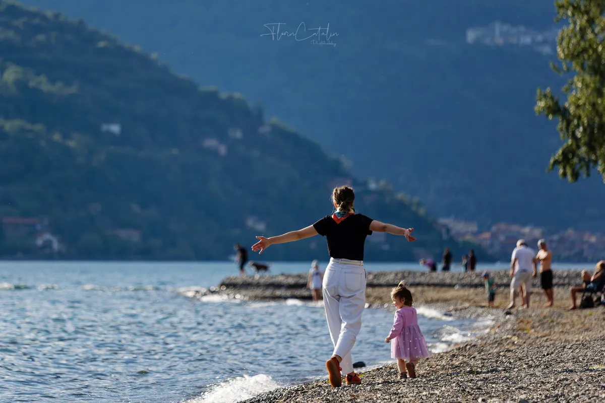 Reise-Fotoshooting am See – Mutter und Kind spazieren am Ufer mit Bergpanorama